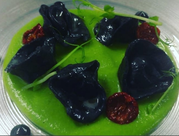 Ravioli al nero con baccalà, crema di piselli, pomodorini confit e germogli di pisello