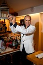 Barman in giacca bianca utilizza uno shaker dietro al bancone del bar dell'Hotel Saraceno, tra bottiglie e bicchieri.